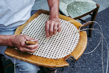Close up sur les mains d'un artisan rempailleur de chaise en train de réparer une chaise en osier