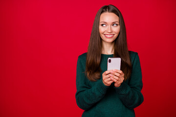 Fototapeta premium Photo of positive girl look copyspace hold smartphone wear green sweater isolated over red shine color background