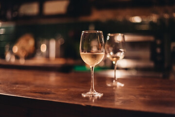 Two glasses of white wine in a dark cozy bar. Wine served on a wooden table