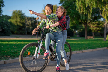 Obraz premium Two pretty young caucasian girls searching the way on a bicycle along the street. Best friends enjoying a day on a bike. Sunny summer evening