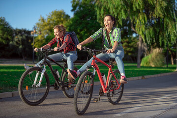 Fototapeta na wymiar Two pretty young caucasian girls having fun on bicycles along the street. Best friends enjoying a day on bikes. Sunny summer evening