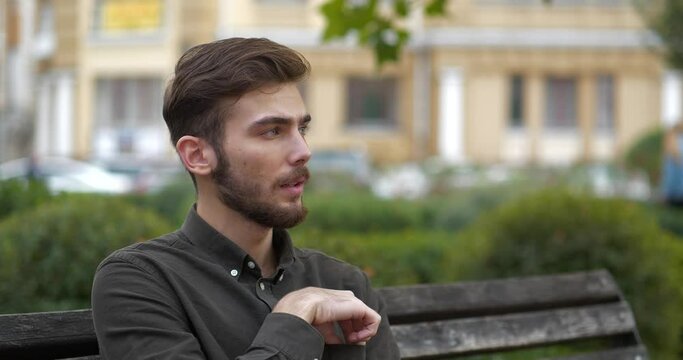 Cinema 4K 60fps Young man sits on the bench in park and puts on medical protective mask. Covid concept health and safety, N1H1 coronavirus quarantine, second wave covid virus protection