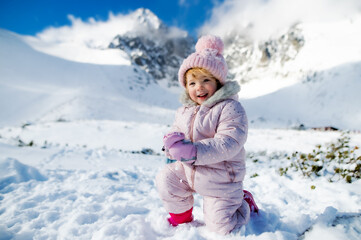Fototapeta na wymiar Portrait of cheerful small girl lying in snow in winter nature, playing.