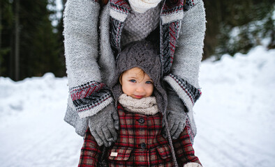 Unrecognizable mother with small daughter standing in winter nature.
