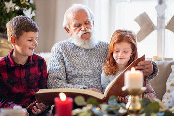 Small children with senior grandfather indoors at home at Christmas, looking at photographs.