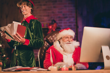 Photo portrait of santa claus browsing internet on desktop and elf holding paper mail