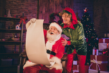 Photo portrait of shocked santa claus and elf reading nice and naughty list together