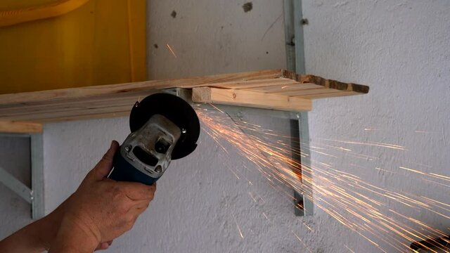 A worker is using an angle grinder to polish steel, sparks are flying everywhere