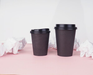two brown paper coffee cups on a pink background, crumpled paper next to them