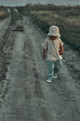 Two-year-old child in a hat walks along a country road, summer. Knowledge of the world.