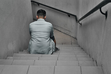 A young guy sits on the steps, view from the back. Underpass, stairs down.