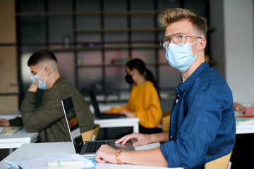 Young students with face masks at desks at college or university, coronavirus concept.