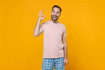 Excited young bearded man in pajamas home wear showing OK gesture looking camera while resting at...