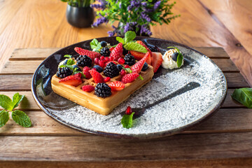 Belgian waffles with strawberries, blueberries, blackberries and syrup, homemade healthy breakfast, toned image, selective focus. Traditional belgian waffles with fresh fruit and whipped cream.