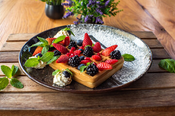 Belgian waffles with strawberries, blueberries, blackberries and syrup, homemade healthy breakfast, toned image, selective focus. Traditional belgian waffles with fresh fruit and whipped cream.