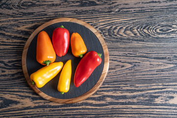 Colored mini peppers. Mixed sweet baby paprika or bell peppers on black plate and wooden table with text space. Top view
