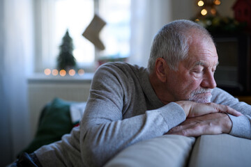 Lonely senior man sitting and sleeping on sofa indoors at Christmas, solitude concept.