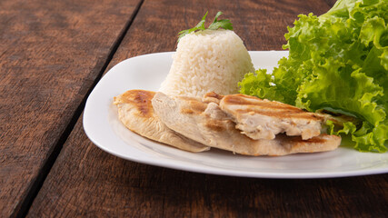 Rice, lettuce and grilled chicken on a white plate, on wooden surface, gray background, selective focus.