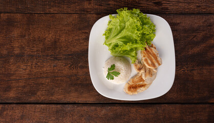Rice, lettuce and grilled chicken on a white plate, on wooden surface, gray background, selective focus.