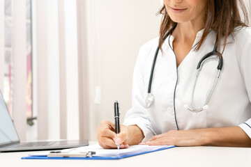 Close-up view on female doctor writing on clipboard.