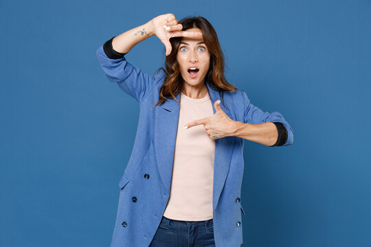 Shocked Amazed Attractive Beautiful Young Brunette Woman 20s In Basic Jacket Standing Looking Camera Making Hands Photo Frame Gesture Isolated On Bright Blue Colour Wall Background Studio Portrait.