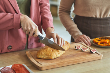 Close up of two unrecognizable women cutting fresh bread while cooking for dinner party, copy space