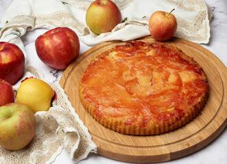 baked round apple pie on wooden board and fresh apples