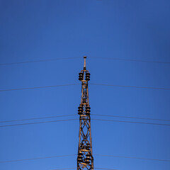Obraz premium Symmetrical photography of the construction of the transmission line for the transmission of high voltage electricity. Behind is a clear blue sky.
