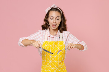Pretty young brunette woman housewife 20s in yellow apron hold knife and fork eating licking lips...