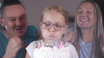 Cute little girl celebration birthday in dark at home. Blowing candles on cake. Six years old. Funny family. Mom and dad are happy for their daughter and laugh. Celebrate and congratulation