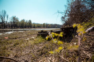 An old wooden boat on the shore, the boat is rotten and no longer for use, and there is a lot of garbage in it and around it, thrown plastic bottles, plastic bags and packaging.