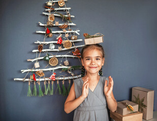 Girl near original Christmas tree made with branches, ecological toys, zero waste holidays
