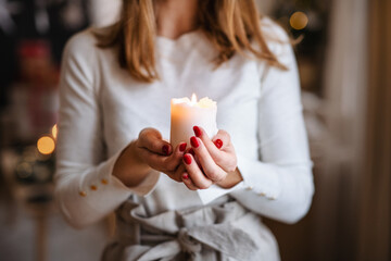 Unrecognizable young woman indoors at home at Christmas, holding candle.