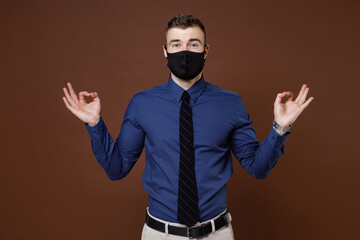 Young business man in shirt mask to safe from coronavirus virus covid-19 hold hands in yoga gesture relaxing meditating isolated on brown background studio. Achievement career wealth business concept.