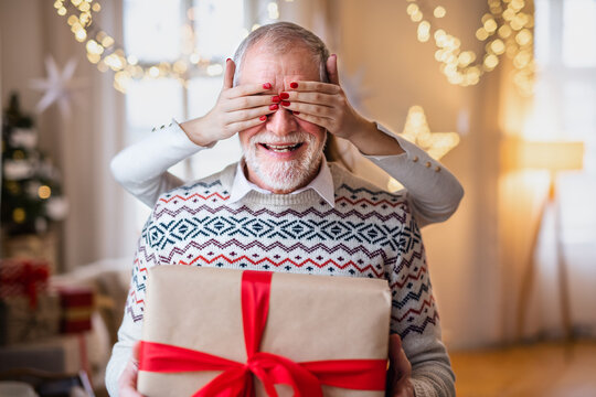 Unrecognizable young woman giving present to senior grandfather indoors at home at Christmas.