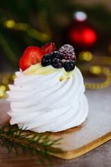 Pavlova cake on a wooden board against the background of a Christmas tree.