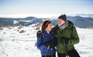 Senior couple hikers with nordic walking poles in snow-covered winter nature.