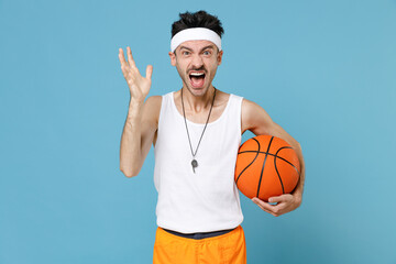 Angry fitness man basketball player with thin skinny body sportsman in headband shirt shorts whistle hold ball screaming swearing isolated on blue background. Workout gym sport motivation concept.