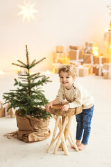 Handsome curly little boy decorated a Christmas tree in a white room