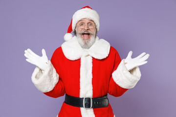 Fototapeta na wymiar Shocked elderly Santa Claus man in Christmas hat red suit coat glasses keeping mouth open spreading hands isolated on violet purple background studio. Happy New Year celebration merry holiday concept.