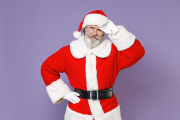 Fototapeta na wymiar Preoccupied displeased tired Santa Claus man in Christmas hat red suit coat gloves glasses put hand on head isolated on violet background studio. Happy New Year celebration merry holiday concept.