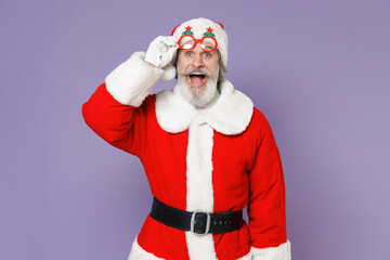 Fototapeta na wymiar Surprised elderly Santa Claus man in Christmas hat red suit coat white gloves glasses keeping mouth open isolated on violet purple background studio. Happy New Year celebration merry holiday concept.