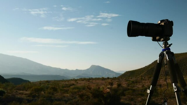 Professional camera on tripod taking travel picture in Tabernas desert, Andalusia Spain. Clouds moving over hills landscape. Time lapse