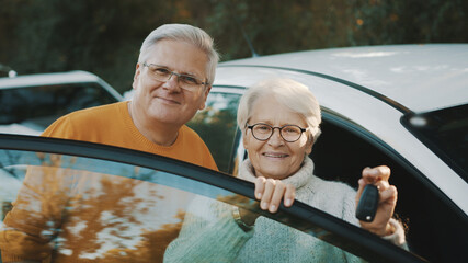 Senior couple purchased new car. Standing near the door and woman holding keys. High quality photo