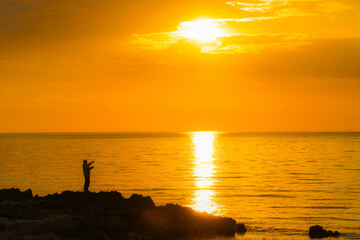 silhouette of a fisherman fishing by the sea at sunset
