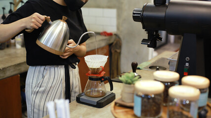 Women barista pouring water to make coffee using manual drip brewer. Hand drip coffee, Barista pouring water on coffee ground with filter