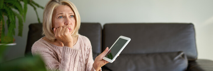 mature woman sitting on couch and using digital tablet. Browsing internet over tablet at home. Middle age woman holding computer at home.