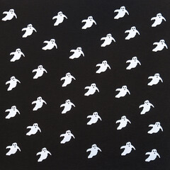 Halloween background. White confetti ghosts on black paper background. Happy Halloween concept. Greeting card, festive backdrop for Halloween holiday. Flat lay, top view