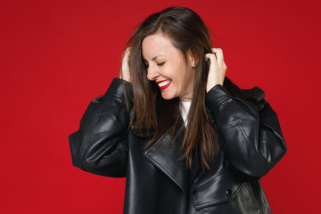 Smiling pretty charming young brunette woman 20s wearing basic casual black leather jacket white t-shirt keeping eyes closed put hands on head isolated on bright red colour background studio portrait.