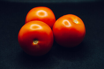 A trio of tomatoes on black background. Shallow focus, blur, red, 3, food prep, contrast, dark, lighting.